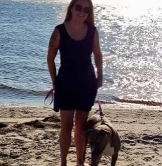 woman wearing sunglasses with a dog on the beach in front of the water
